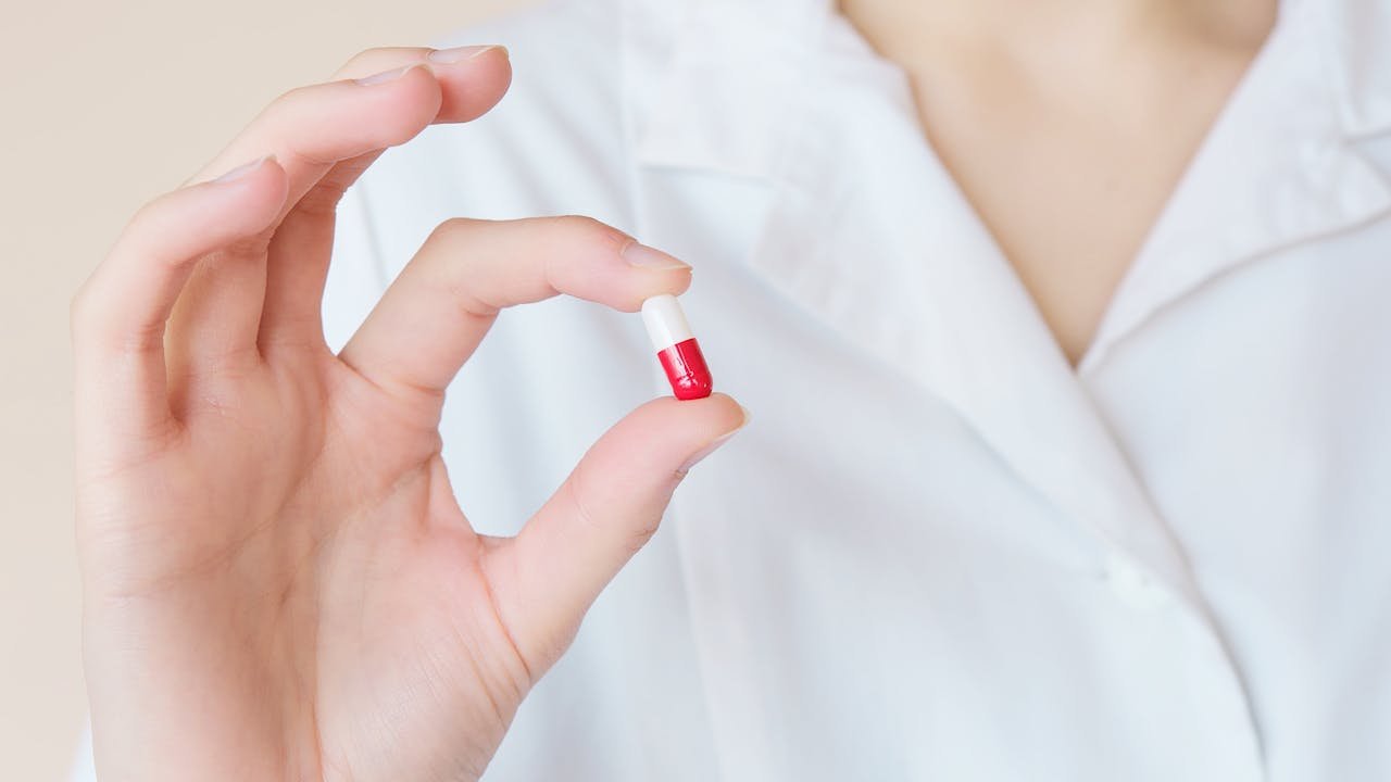 A healthcare professional holds a red and white capsule, exemplifying modern medicine.